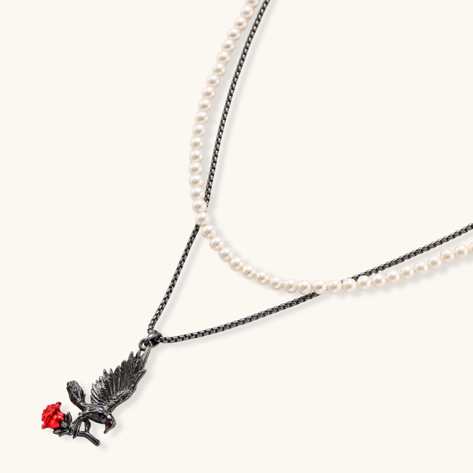 Gothic eagle pendant carrying red rose on black chain layered with white pearls against cream background